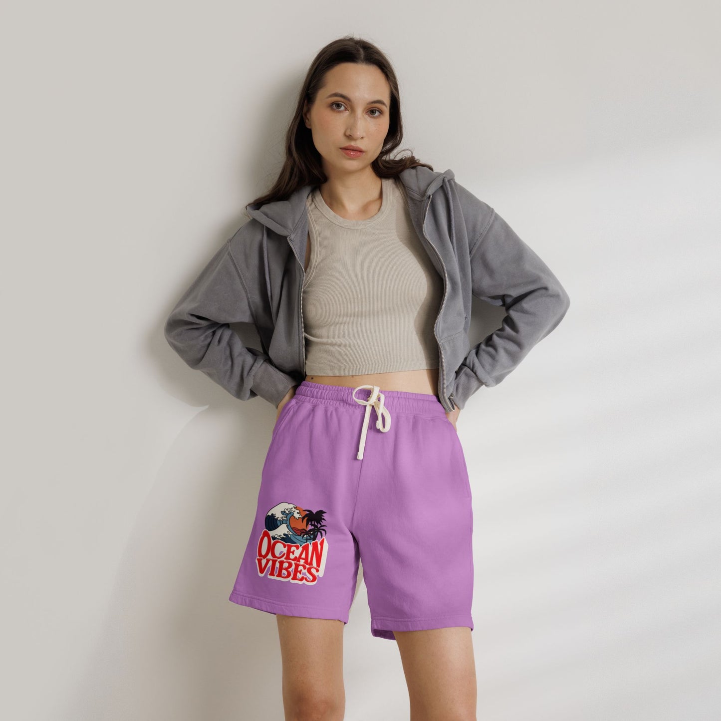 A woman stands against a light gray wall wearing purple drawstring shorts with a colorful 'Ocean Vibes' graphic on the left leg, a beige crop top, and a gray zip-up hoodie. Unique Lightweight Fleece Sweat Shorts in Ocean Vibes Graphic Shop Lightweight Fleece Sweat Shorts in Ocean Vibes for breezy comfort, relaxed style, and an easygoing summer-ready look all day. Refresh your casual rotation with Lightweight Fleece Sweat Shorts in Ocean Vibes—soft, versatile, and ready for sunny days by the shore.
