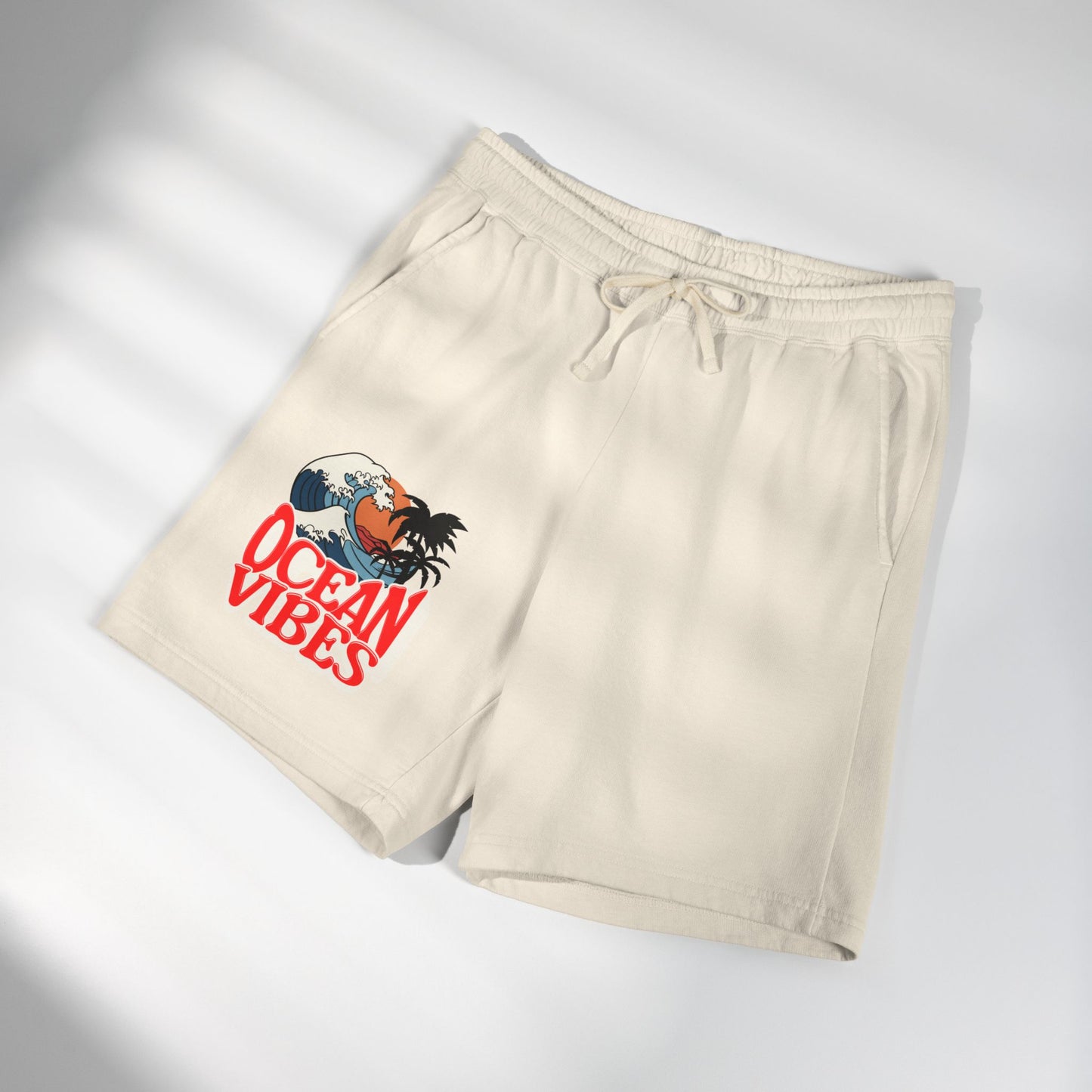 Beige drawstring shorts with a graphic print on the left leg featuring a rooster and the text 'OCEAN VIBES' in red, shown on a white background with soft diagonal shadows.