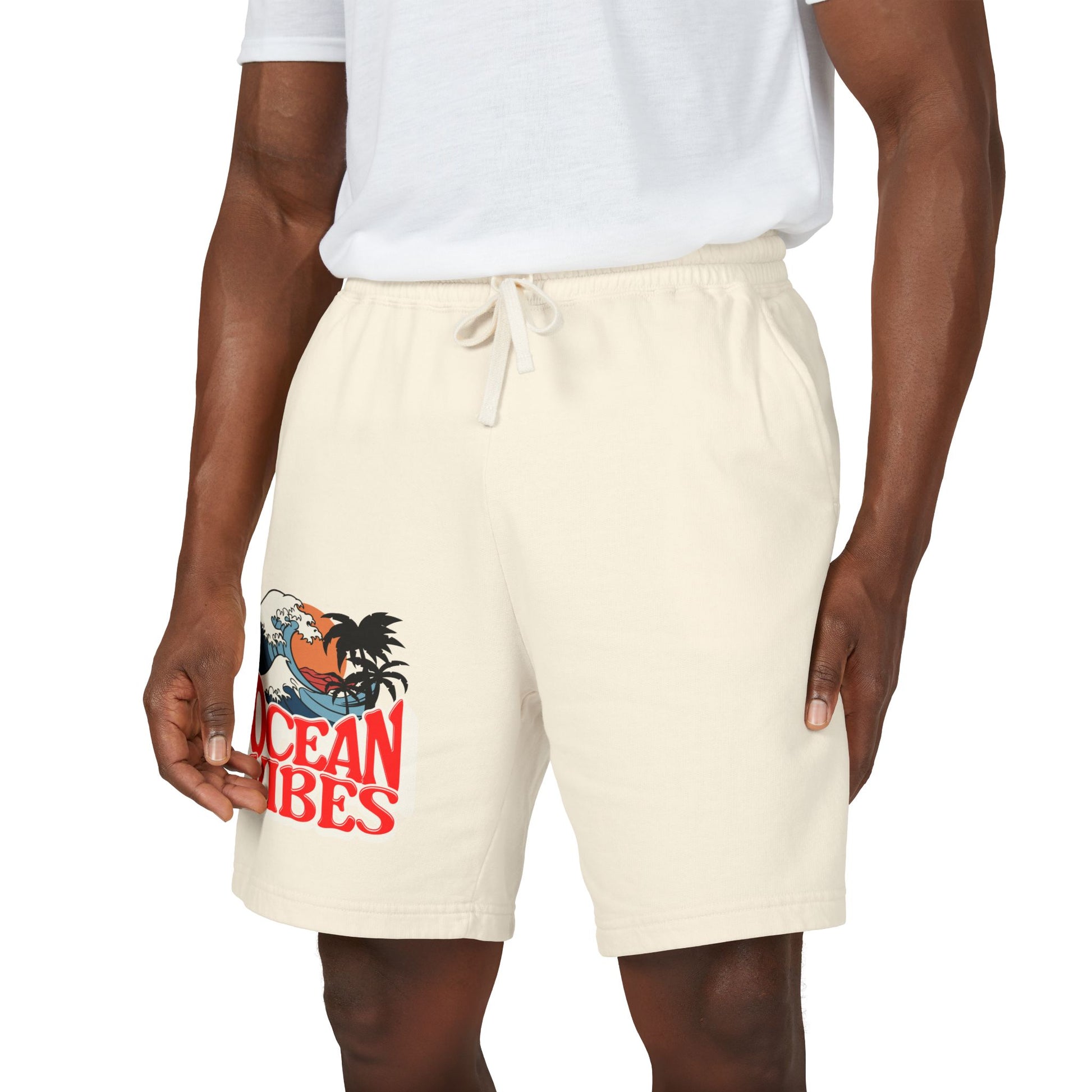 A model wearing off-white drawstring shorts with a graphic print of a rooster on a wave and the text 'OCEANribes' in red, paired with a white t-shirt against a white background. Unique Lightweight Fleece Sweat Shorts in Ocean Vibes Graphic Shop Lightweight Fleece Sweat Shorts in Ocean Vibes for breezy comfort, relaxed style, and an easygoing summer-ready look all day. Refresh your casual rotation with Lightweight Fleece Sweat Shorts in Ocean Vibes—soft, versatile, and ready for sunny days by the shore.