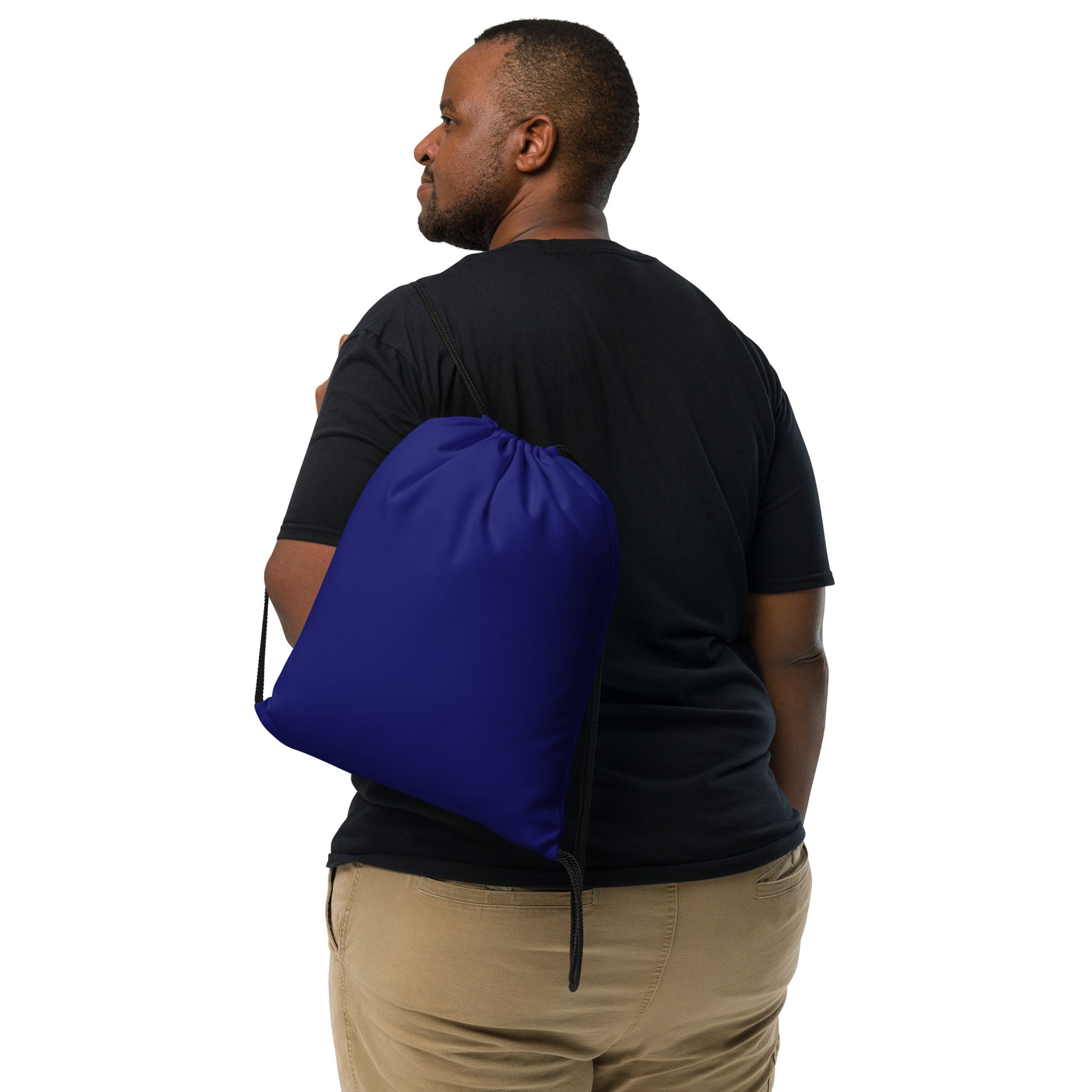 A man shown from the back wearing a black t-shirt and khaki pants, carrying a royal blue drawstring gym bag over his shoulder against a solid white background. Bold Compact Minimalist Solid Midnight Blue Drawstring Bag