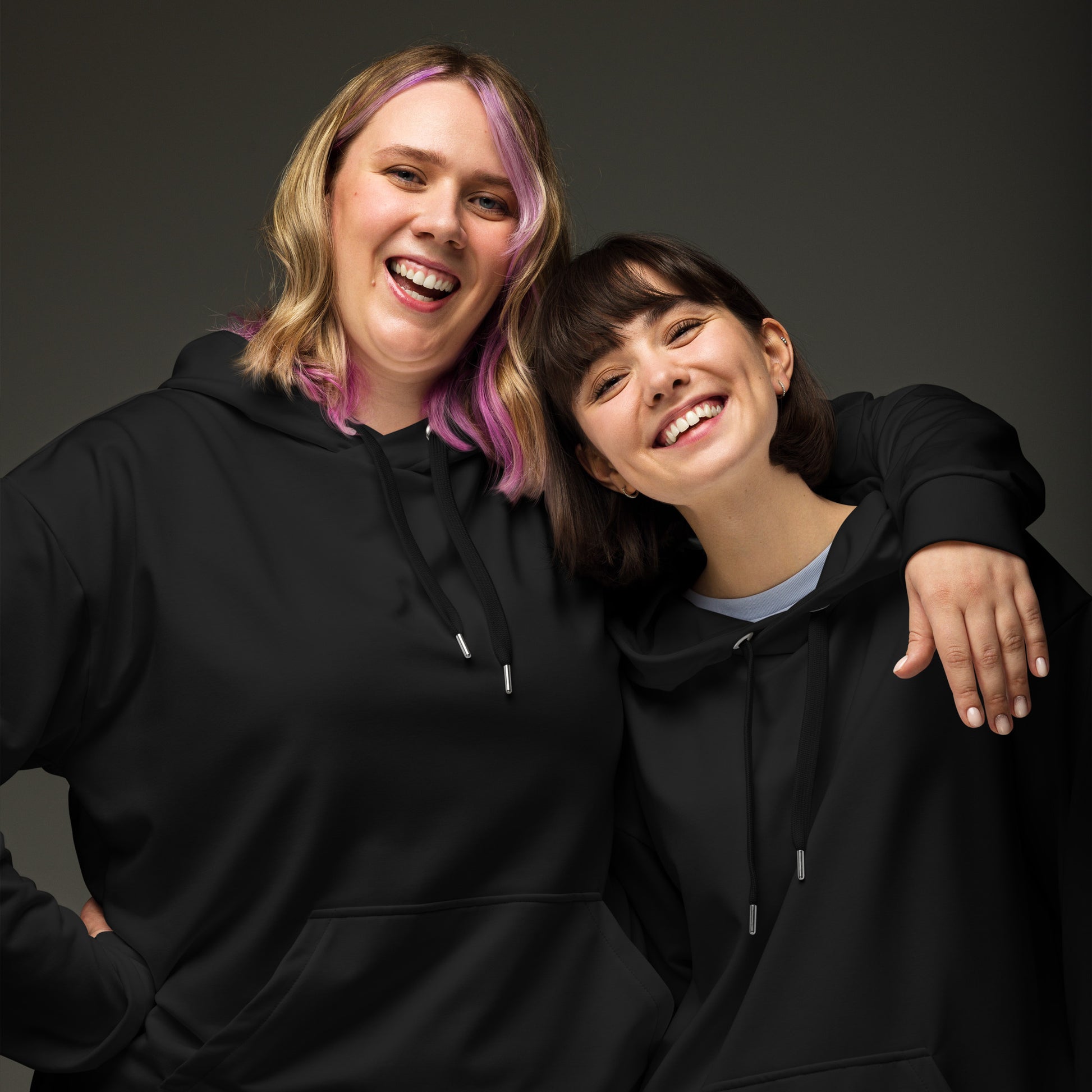 Two women smiling and posing together while wearing matching black hoodies against a dark gray studio background. Comfortable Minimalist Bold Plain Midnight Black Hoodie for Relaxed Wear