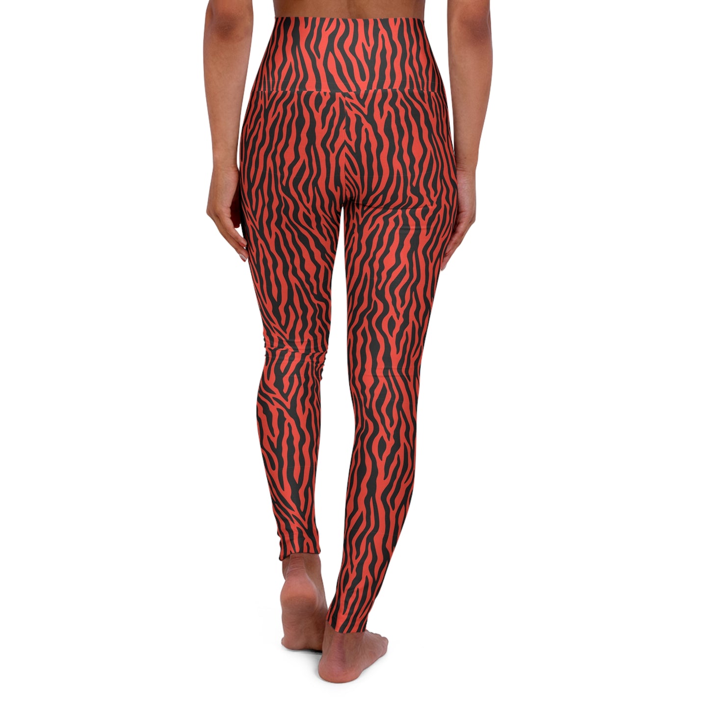 Rear view of a person wearing high-waisted leggings with a bold red and black zebra-like stripe pattern, standing barefoot against a plain white background. Comfortable Yoga Wear Featuring Tiger Print Design
