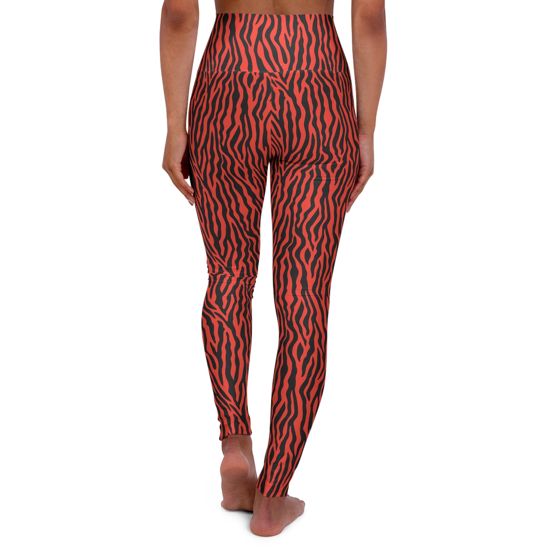 Rear view of a person wearing high-waisted leggings with a bold red and black zebra-like stripe pattern, standing barefoot against a plain white background. Comfortable Yoga Wear Featuring Tiger Print Design