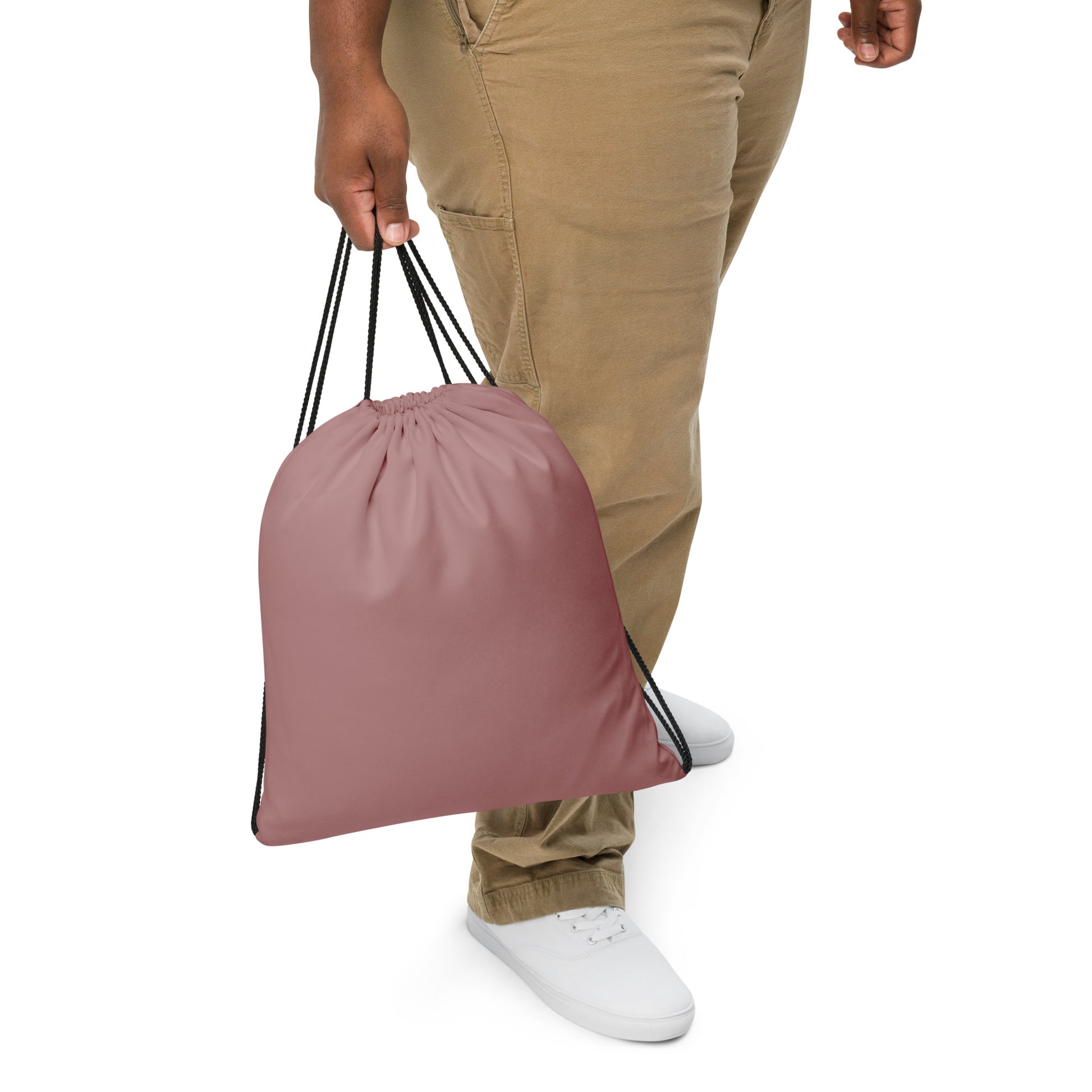 A person wearing khaki pants and white sneakers holds a dusty rose drawstring bag against a clean white background. Sleek Minimalist Solid Rosy Brown Durable Drawstring Bag